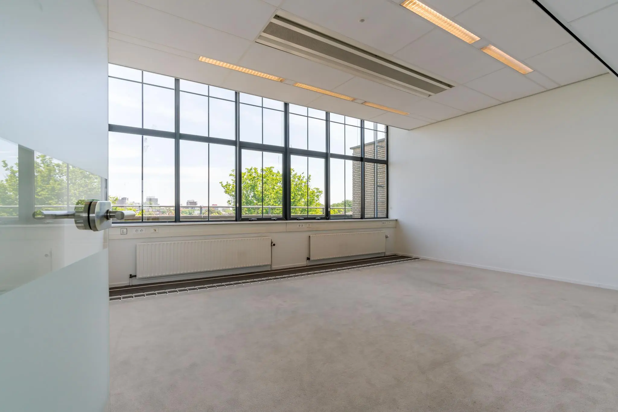 Licht en leeg kantoor aan de Van Alkemadelaan met grote ramen en uitzicht op groen.